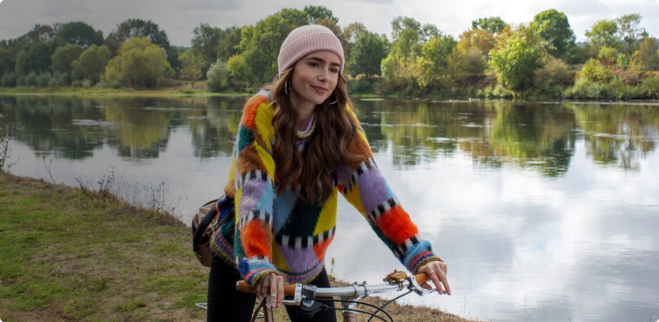 Emily in paris riding a bike near a lake